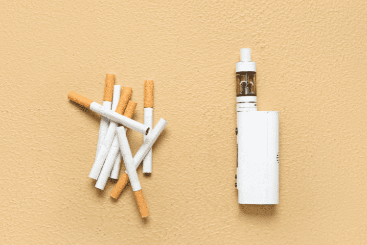 Several traditional cigarettes placed beside a white vape device on a beige background.