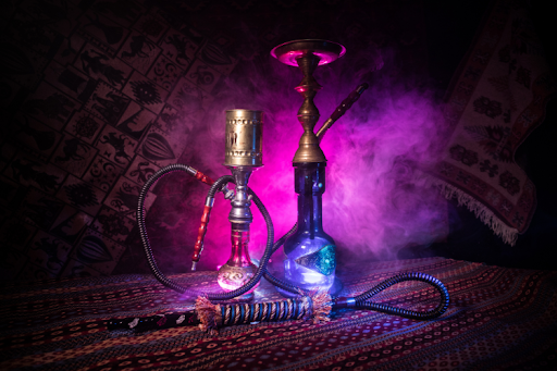 A hookah and a glass pipe with swirling smoke rising from them, set against a soft background.