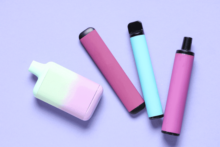 Mix of pastel-colored vape pens and pods on a light purple background.