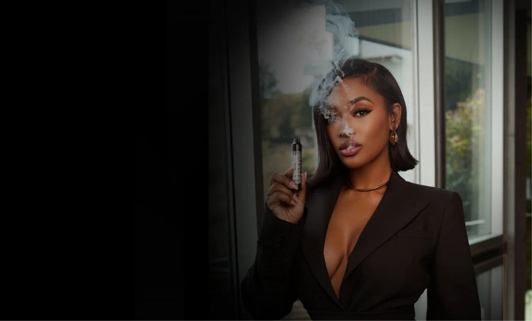 A confident woman in a sleek black suit exhales vapor while holding a vape pen.