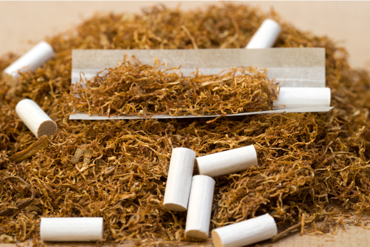 Loose tobacco with rolling paper and cigarette filters arranged on a flat surface.